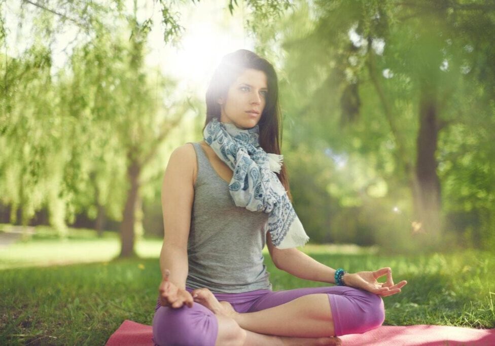 Portrait of beautiful mixed race caucasian, african, middle eastern girl meditating and doing yoga at sunset on the grass in a park or forrest