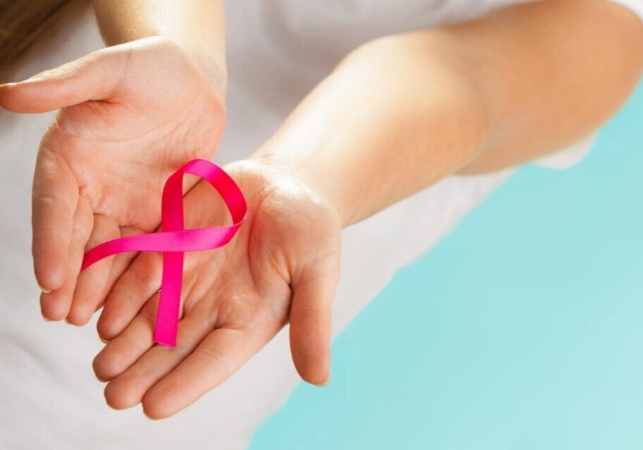 healthcare and medicine concept - woman hands holding pink breast cancer awareness ribbon on blue